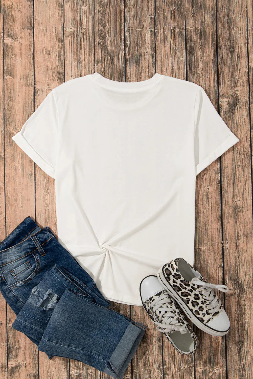 White round neck short sleeve T-shirt styled with distressed jeans and leopard print sneakers on a wooden surface.